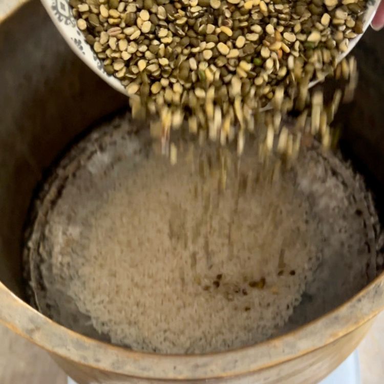 White rice and split green moong dal being combined in a bowl before rinsing.