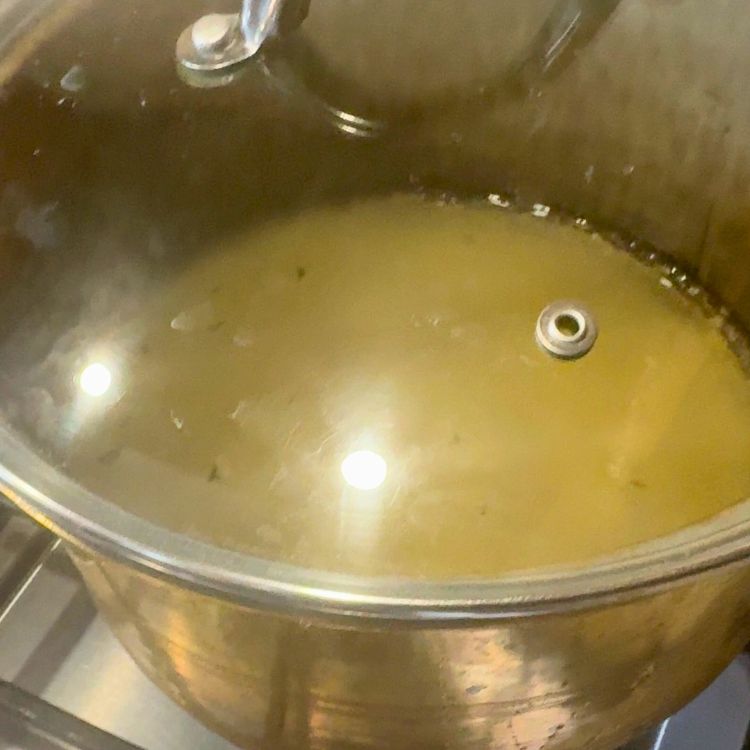 Pot with a lid on a stovetop, simmering high-protein rice with chicken broth.
