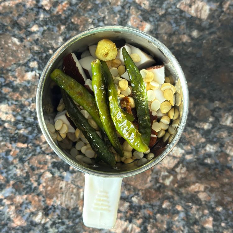 Fresh coconut, chilies, roasted chana dal, and spices added to a blender for coconut chutney preparation.