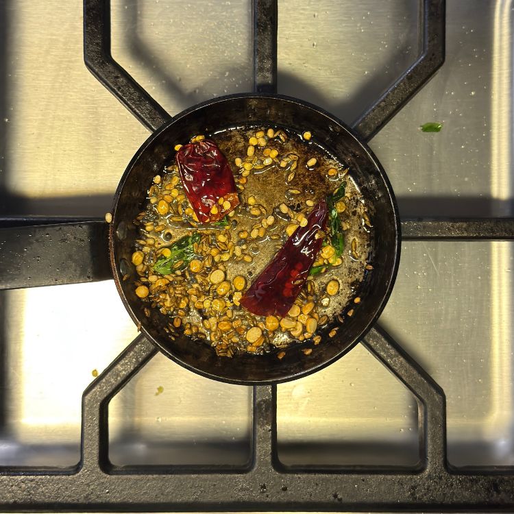 Mustard seeds, curry leaves, and dried red chilies sizzling in oil for coconut chutney tempering.
