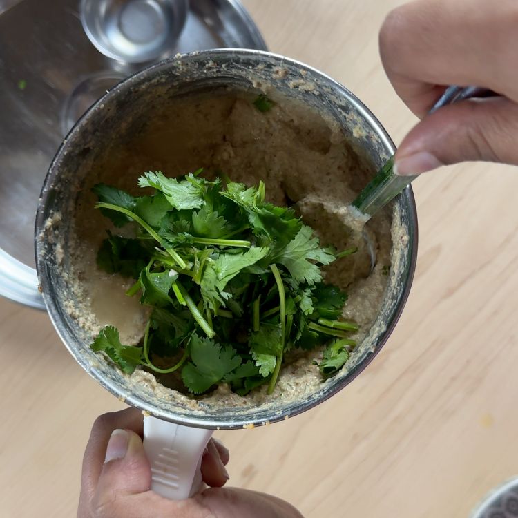 Fresh cilantro being added to creamy peanut chutney paste, enhancing flavor and color