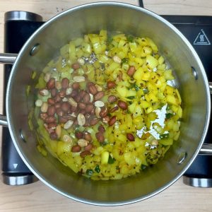 Roasted peanuts being added to the aromatic base of onions and spices, adding texture and protein to homemade upma.