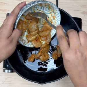 Marinated shrimp being added to a hot pan with sizzling oil and curry leaves starting to splutter