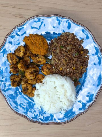 Overhead view of a colorful Indian thali featuring protein rice, carrot chutney, spiced shrimp fry, and horsegram snack arranged on a traditional plate