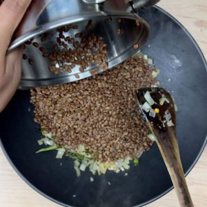 Adding protein-rich cooked horsegram to tempered spices and onions in a pan, bringing together the key elements of this healthy snack.