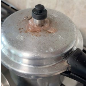 Raw horsegram being cooked in a pressure cooker with water and salt, an essential step for preparing tempered horsegram snack.