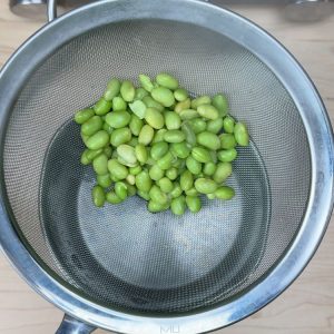 Draining boiled edamame in a metal strainer over the sink