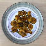 Crispy golden Indian spiced shrimp fry served on a white plate with fresh curry leaves garnish on a wooden table