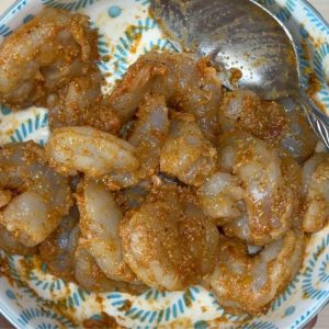 Shrimp coated in a vibrant orange-red spice marinade with visible specks of ginger garlic paste in a glass mixing bowl