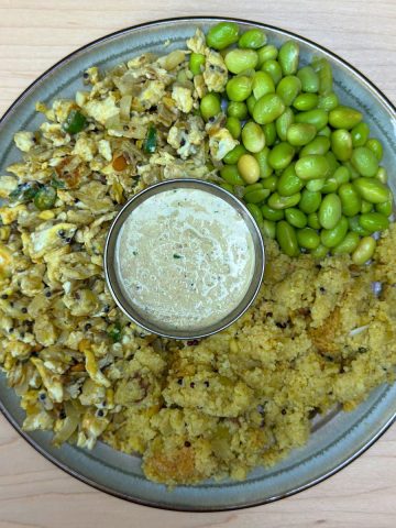 Traditional South Indian upma thali served on a banana leaf with fluffy upma, peanut chutney, egg bhurji, and boiled edamame, showcasing a balanced and nutritious meal with vibrant colors and variety.