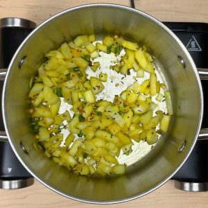 Sautéed onions and diced green chilies cooking with bright yellow turmeric powder in a pan for traditional upma preparation.
