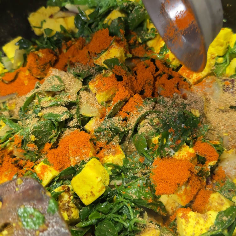A mix of red chili, coriander, and cumin powders being added to the methi and paneer in the pan, perfecting the Methi Paneer Stir Fry seasoning.