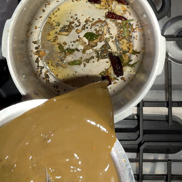 Pouring prepared horsegram water into the tempered spices