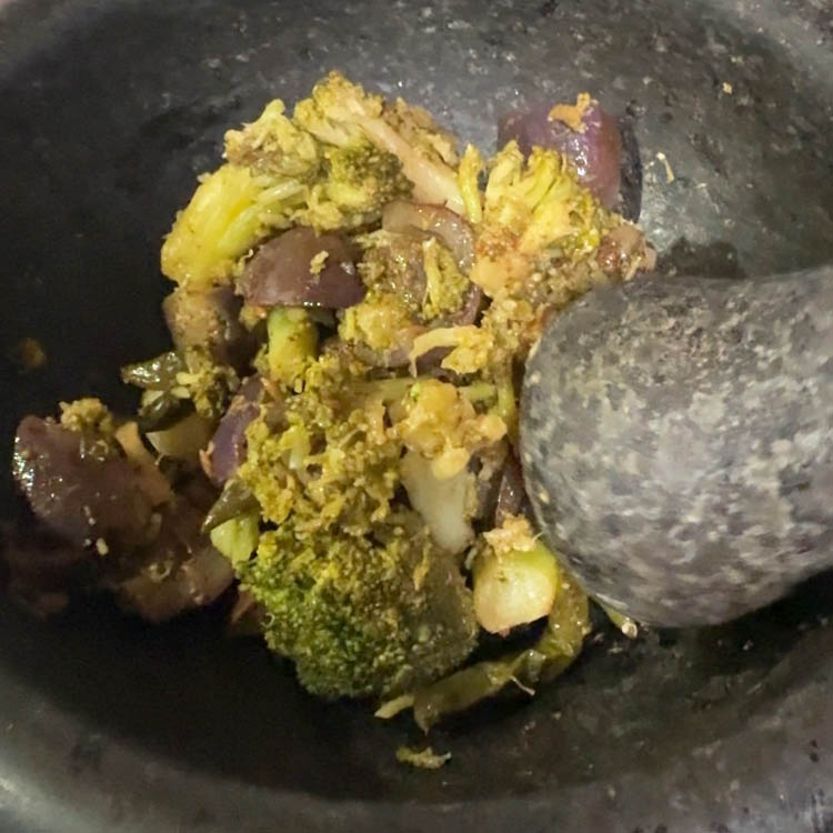 Using mortar and pestle to break down cooked vegetables for authentic broccoli chutney texture