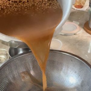 Straining cooked horsegram water into a bowl after pressure cooking the lentils