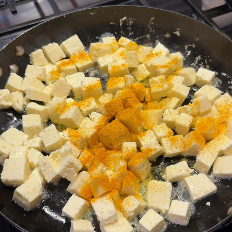 A sprinkle of turmeric powder being added to sautéing paneer in a pan, enhancing the flavor of the Methi Paneer Stir Fry.