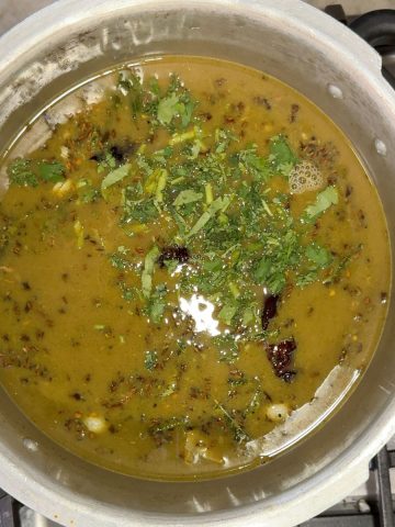 Steaming hot Ulavacharu Rasam served in a traditional brass bowl garnished with fresh cilantro leaves
