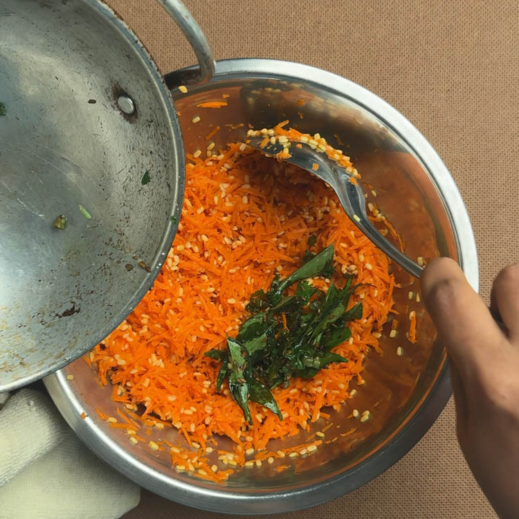 Hot coconut oil tempering being poured over fresh carrot and moong dal mixture for kosambari salad