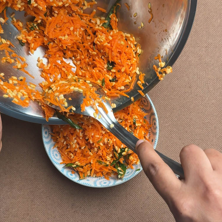 Colorful carrot moong dal kosambari being transferred to a serving bowl, showing crunchy texture