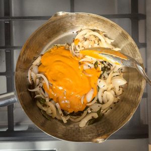 Thick spice paste being stirred into caramelized onions