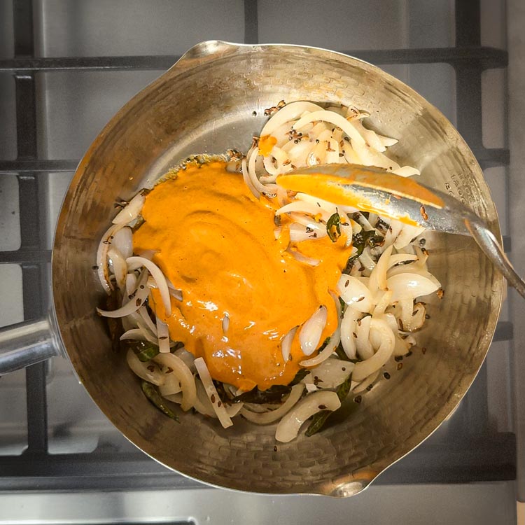 Thick spice paste being stirred into caramelized onions