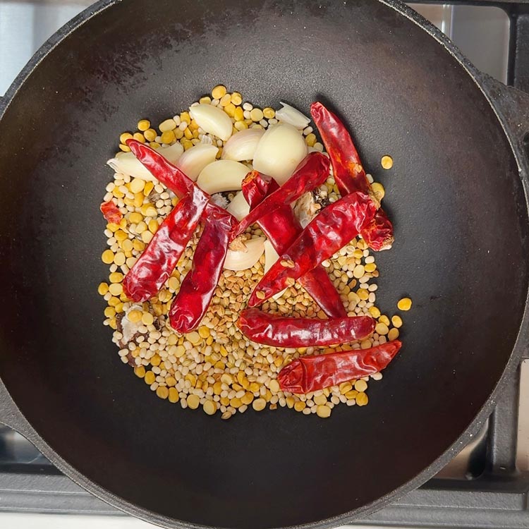 Red chilies, garlic cloves, and whole spices being added to hot pan with golden lentils