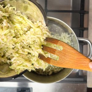 Hand adding white grated vegetable shreds into bubbling water in stainless steel pot