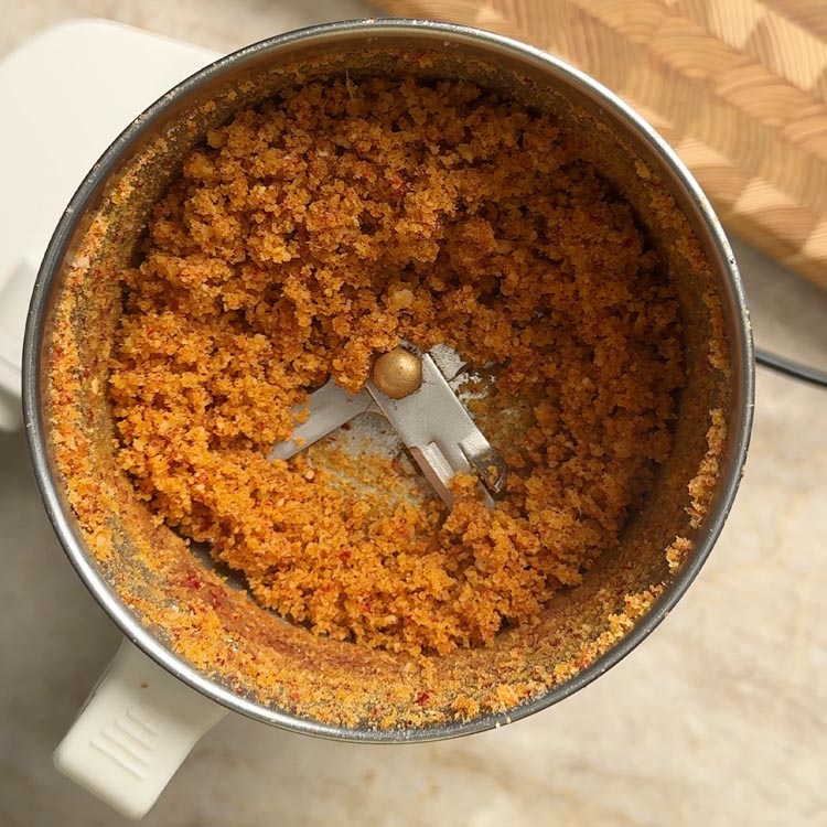 Freshly ground coconut garlic podi showing coarse powder texture inside the mixi jar