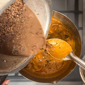 Cooked lentils being added to simmering gravy in pan