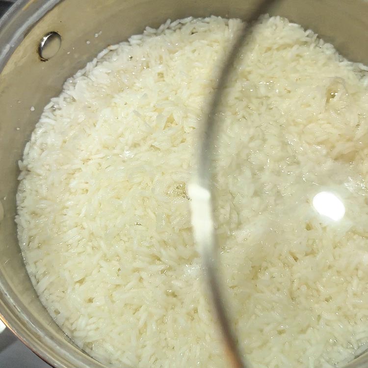 Hand placing lid on pot of white rice ready to simmer