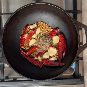 Small brown cumin seeds being sprinkled into pan with other roasted whole spices