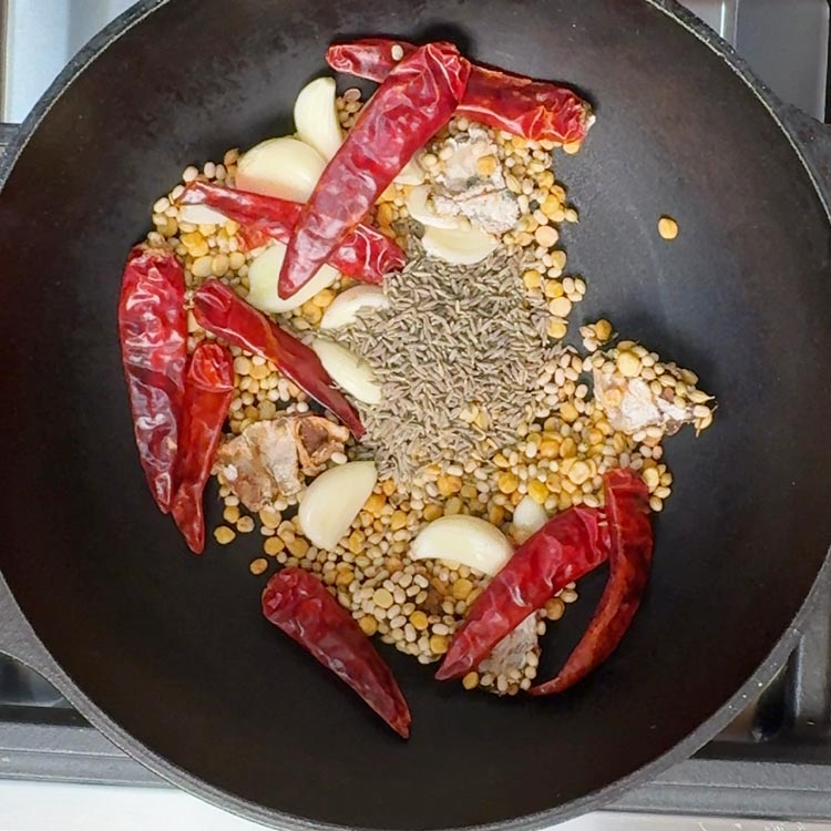 Brown cumin seeds scattered over aromatic spice mixture in cooking pan