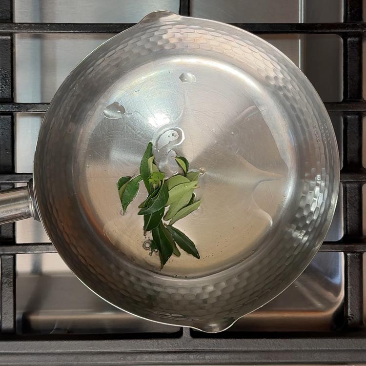 Fresh green curry leaves sizzling and sputtering in hot oil in a heavy-bottomed pan