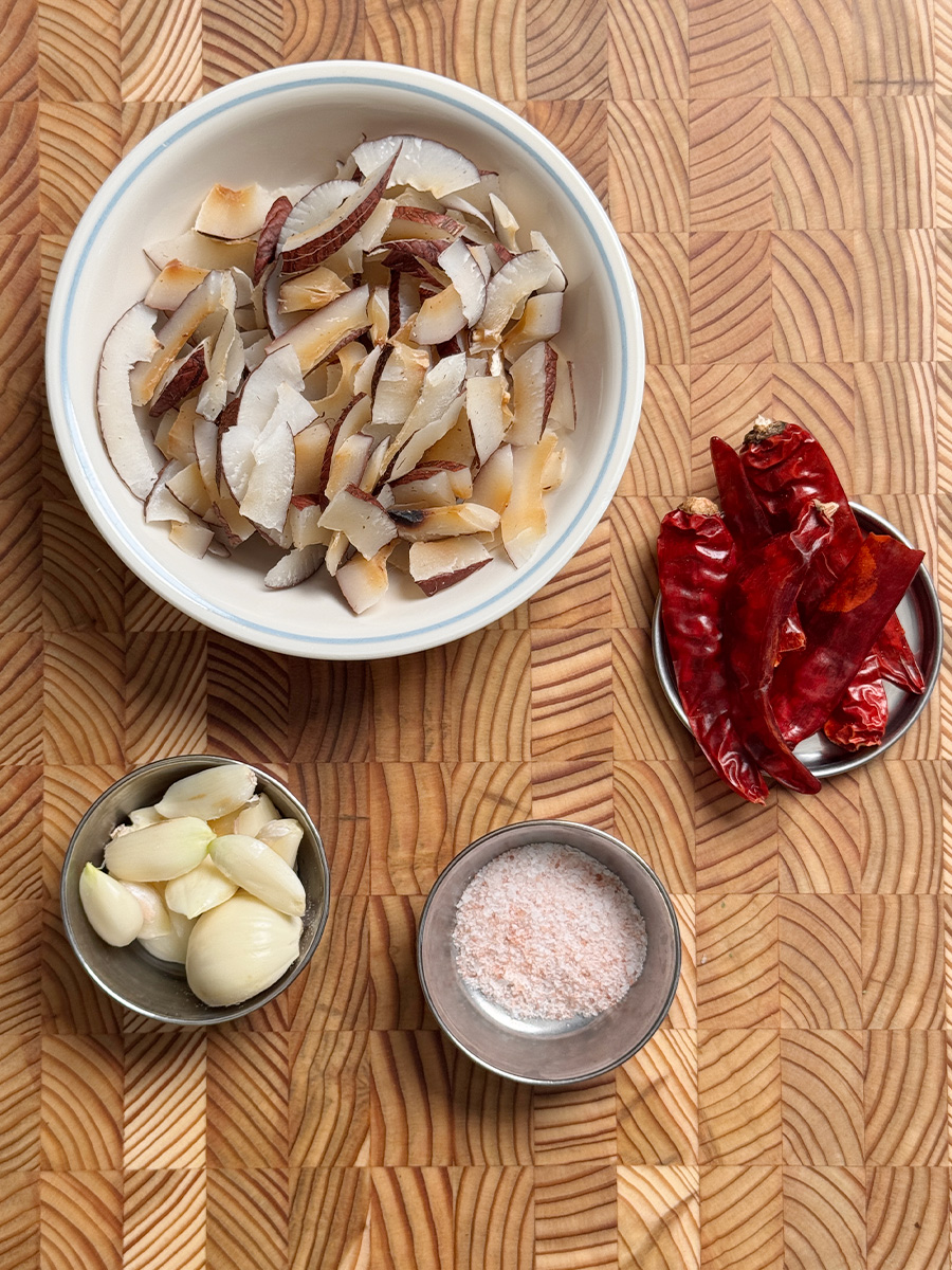 Dried coconut slices, peeled garlic cloves, red chilies and salt arranged on a white background