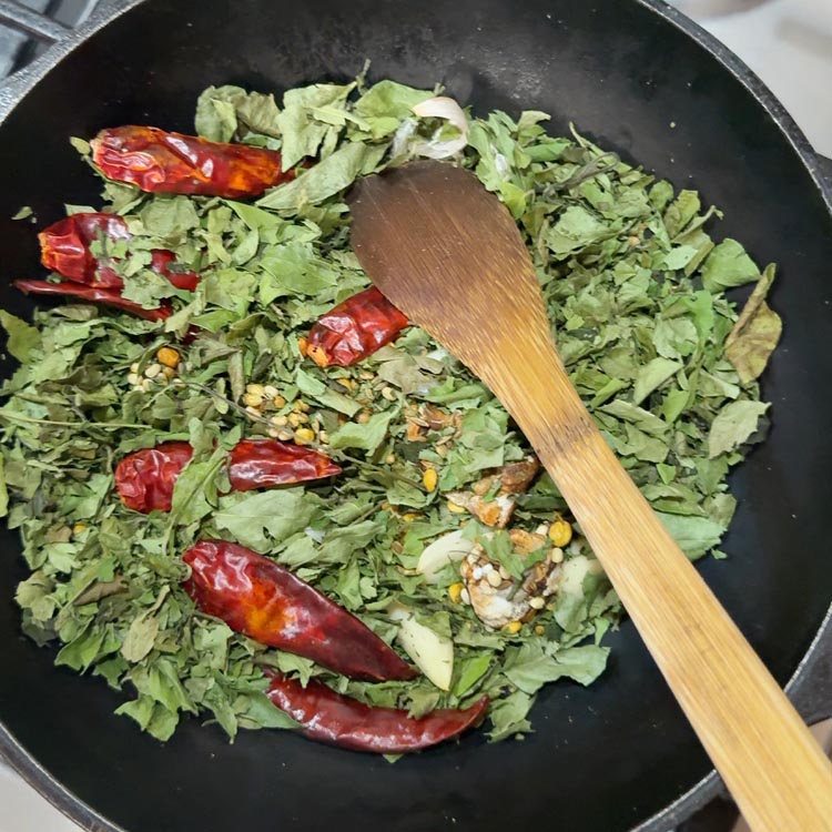 Dark green dried curry leaves being stirred into hot roasted spice mixture