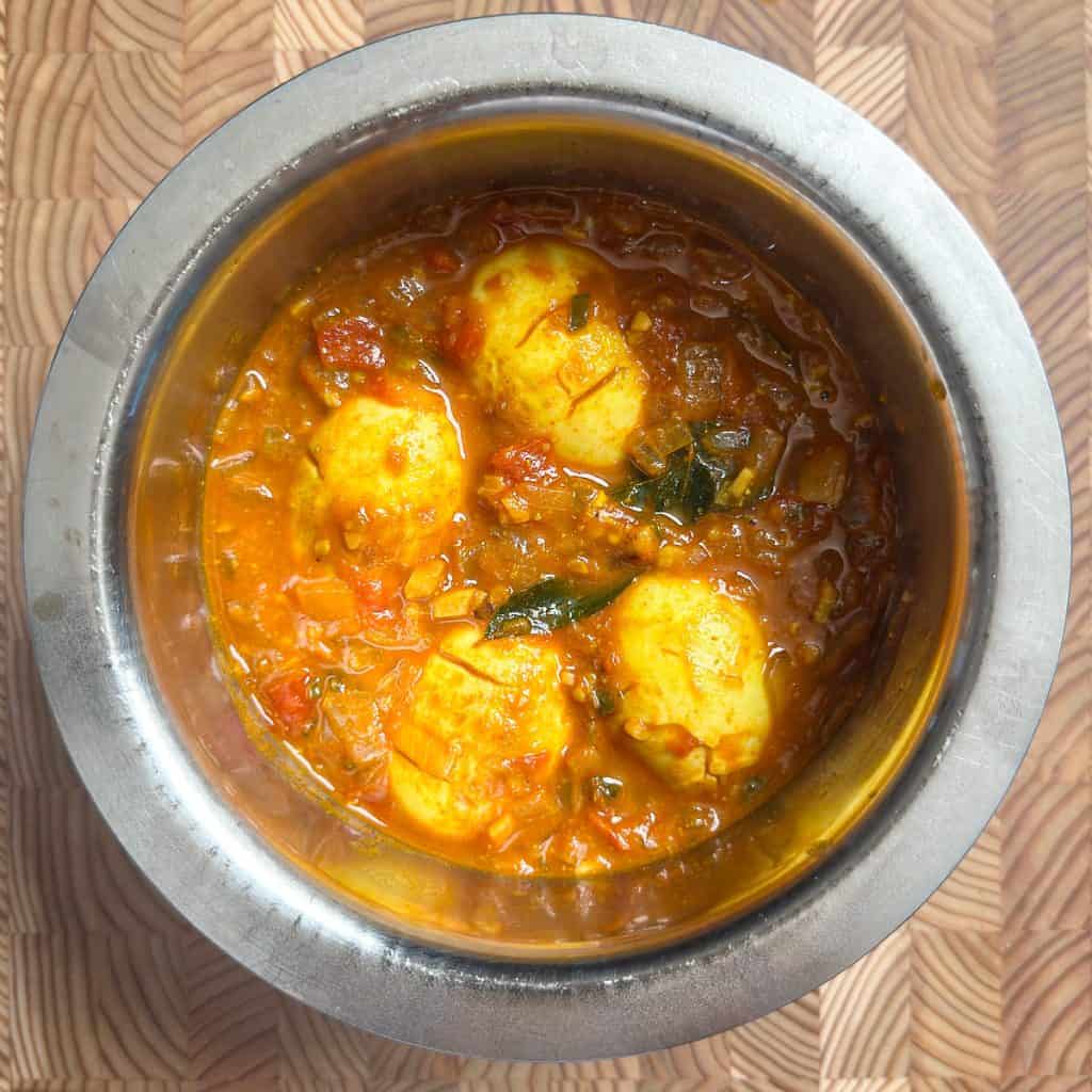 Completed egg pulusu served in a ceramic bowl, garnished with fresh curry leaves