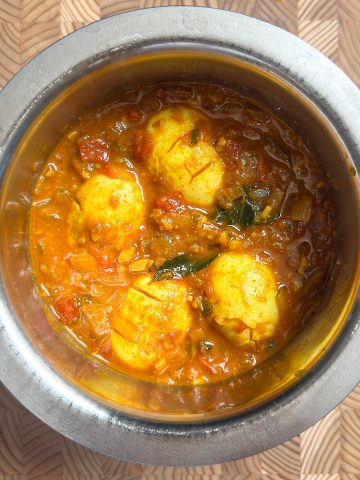 Completed egg pulusu served in a ceramic bowl, garnished with fresh curry leaves