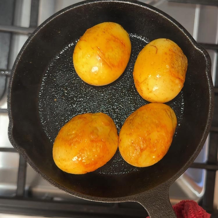 Four golden-brown pan-fried boiled eggs with shallow cuts, coated in turmeric
