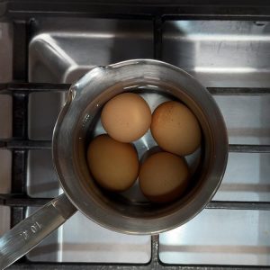 Four eggs boiling in water in a stainless steel saucepan on stovetop