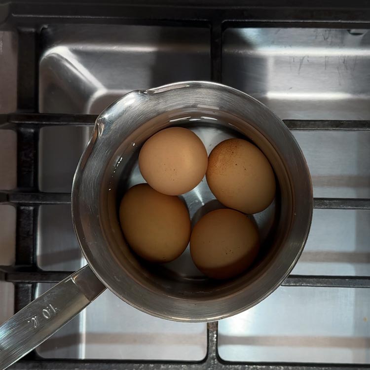 Four eggs boiling in bubbling water in a stainless steel saucepan on stovetop