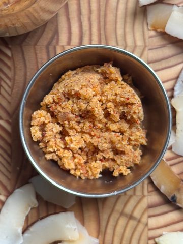 Golden brown coconut garlic podi served in a stainless steel bowl on wooden cutting board