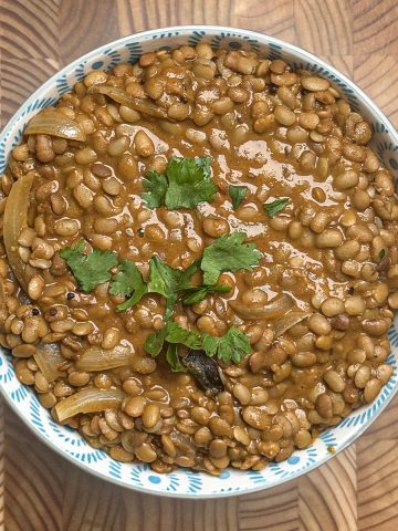 Creamy horse gram curry garnished with fresh herbs in ceramic bowl