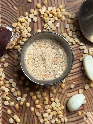 Fine reddish-brown Kandi Podi powder in small ceramic bowl on wooden table, ready to serve with rice