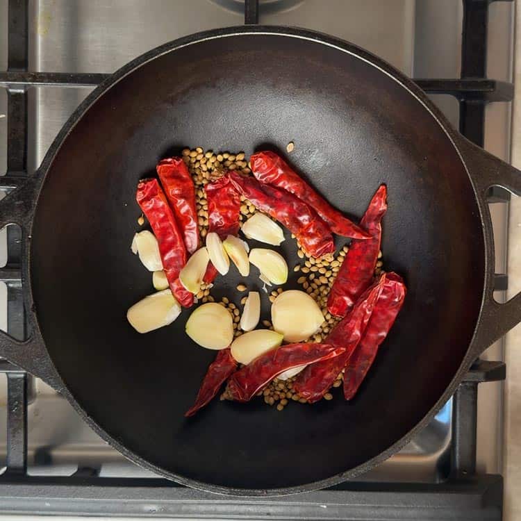 Cumin seeds, coriander seeds, fenugreek seeds, red chilies, and garlic cloves sizzling in hot pan for Kandi Podi recipe
