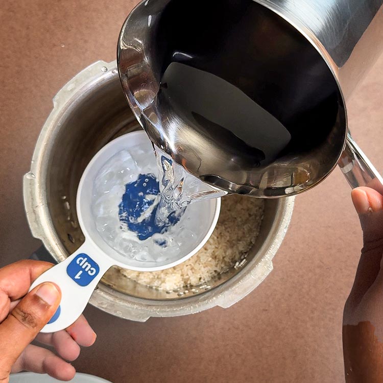 Pouring water from measuring cup into traditional pressure cooker