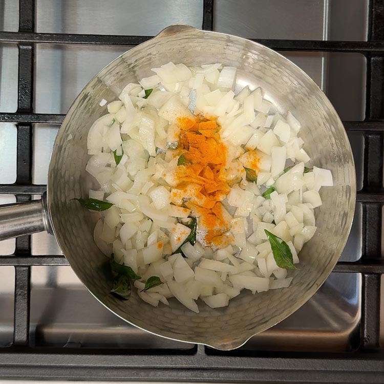 Diced white onions mixed with golden turmeric powder cooking in oil until translucent