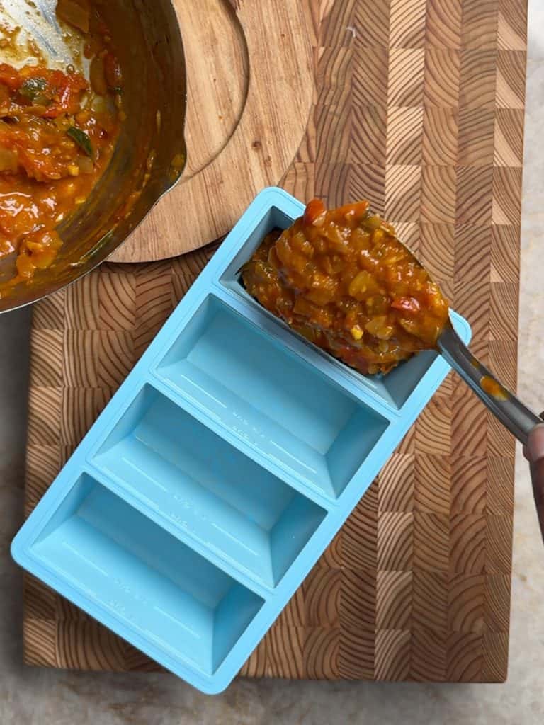 pouring tamarind onion tomato base in a freezing tray with a steel spoon