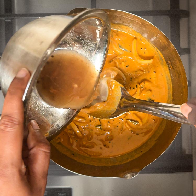 Dark tamarind liquid being poured into bubbling horse gram curry base