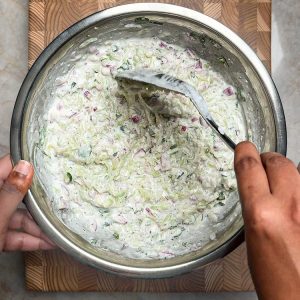 Wooden spoon folding vegetables and herbs into creamy white yogurt mixture