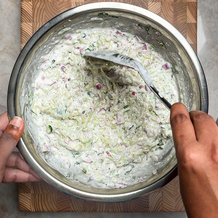 Wooden spoon folding vegetables and herbs into creamy white yogurt mixture